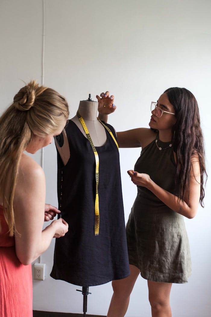 Two women working on dressmaking with a mannequin indoors.